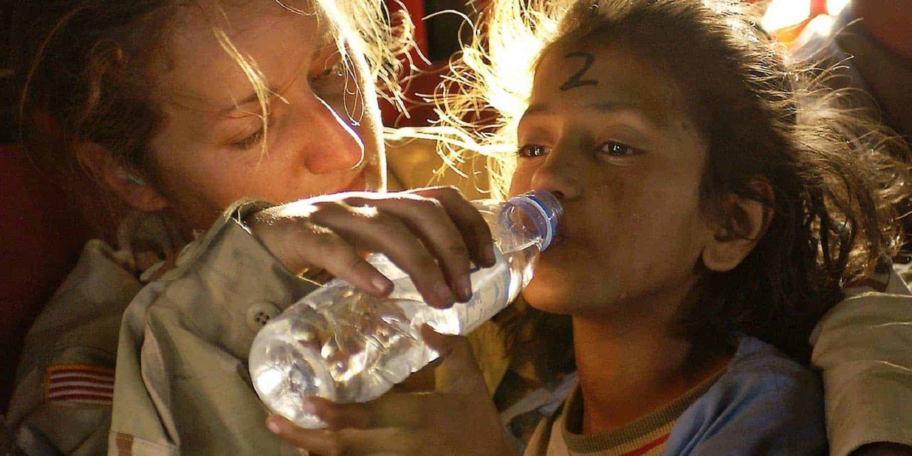 young refugee girl receiving water at a refugee camp