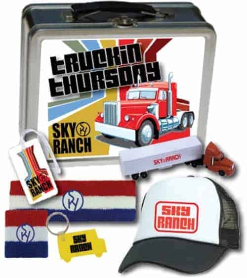 Image of a camper pack for Sky Ranch's Truckin' Thursday event. The pack includes a lunch box, trucker hat, toy truck, sweatbands, keychain, and luggage tag, all branded for Truckin' Thursday.